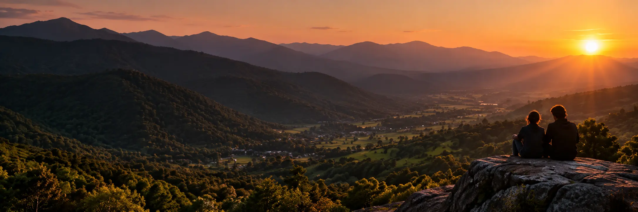 Sunset over the mountains, with two people looking toward the horizon